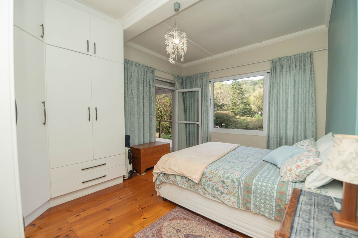 A well-lit bedroom featuring polished timber flooring, ample built-in cupboard storage, and direct access to an outdoor area through a glass door.