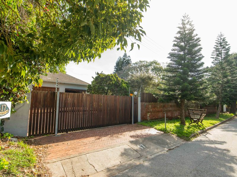 Front exterior view featuring a timber slat gate, electric fencing, and a herringbone brick driveway leading to the property entrance.