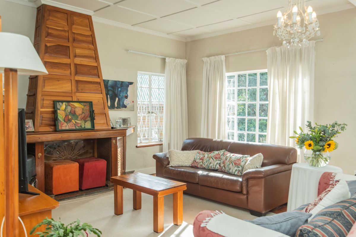 A cozy living room featuring a prominent wooden fireplace surround, classic multi-pane windows, and a decorative crystal chandelier.