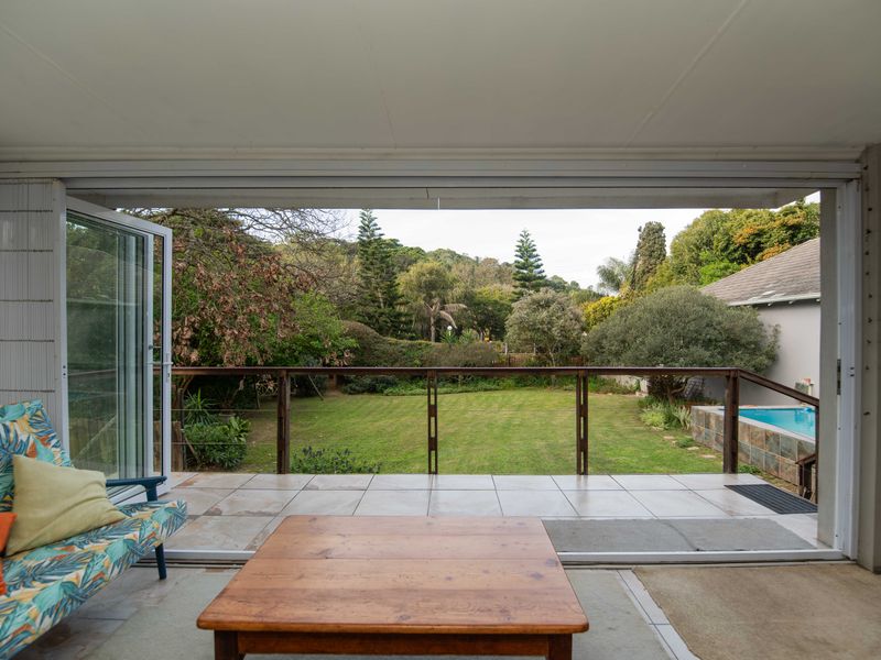 A covered patio featuring tiled flooring and folding glass doors that open onto a spacious garden with a swimming pool.
