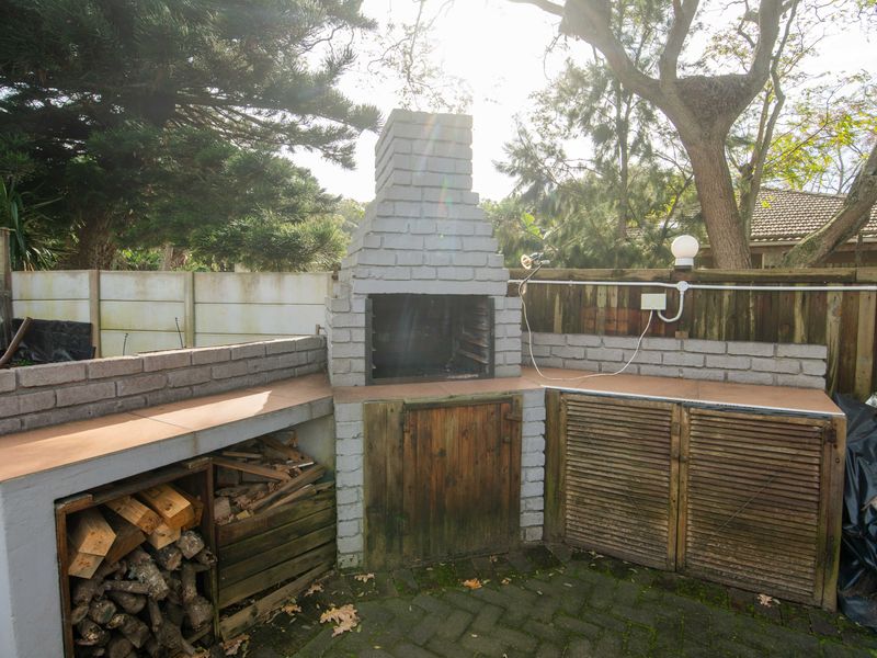 Outdoor patio area featuring a built-in brick braai, masonry counter space with tiled surfaces, and integrated storage cabinets, set within a private garden space.
