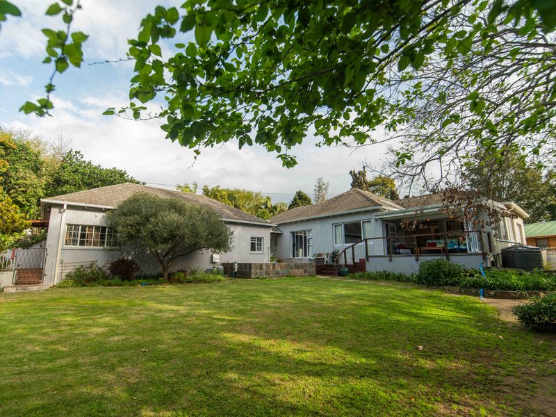 Rear view of the house featuring a spacious lawn, raised patio area with timber decking, and stone-clad retaining wall.