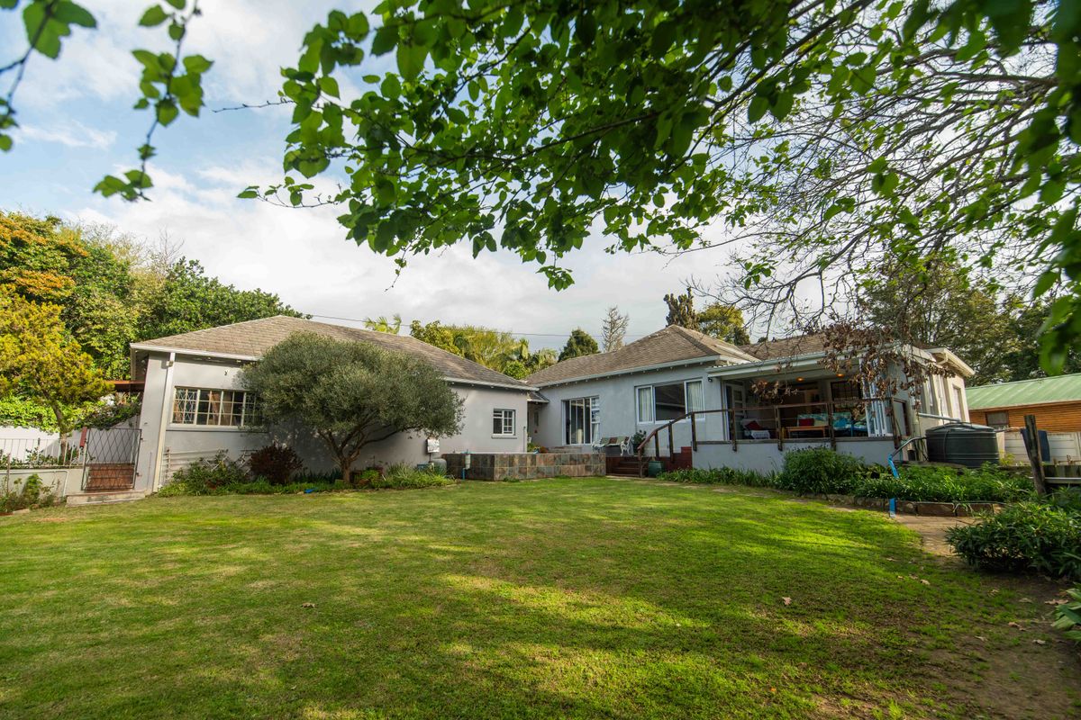 Rear view of the house featuring a spacious lawn, raised patio area with timber decking, and stone-clad retaining wall.