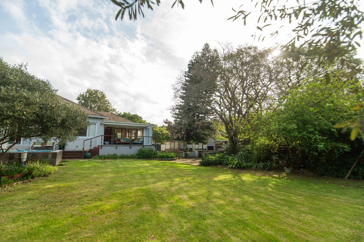 Spacious rear garden featuring a raised patio with timber decking, a built-in braai area, and a swimming pool set within a mature landscaped yard.