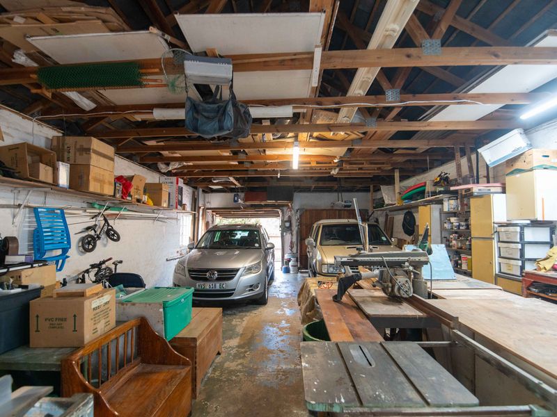 Spacious garage featuring exposed timber roof trusses, concrete flooring, and ample built-in shelving, offering significant potential for workshop or storage use.
