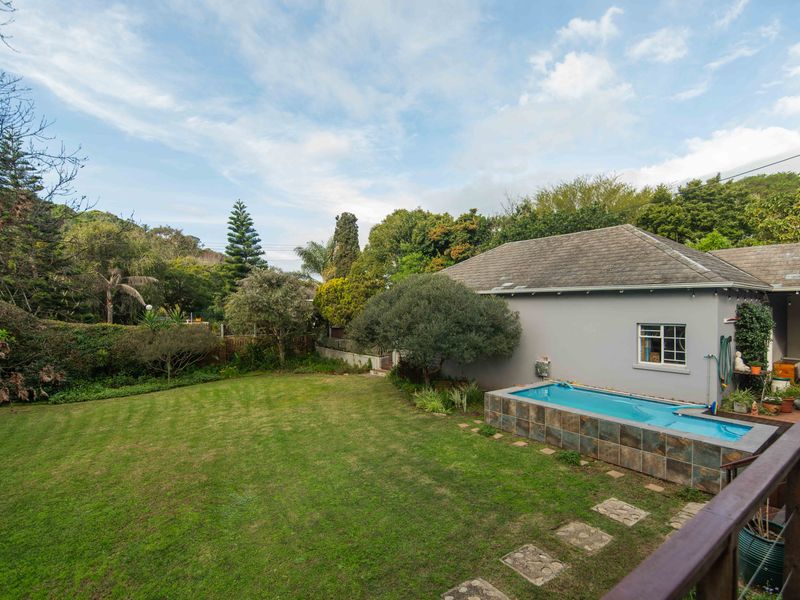 A well-maintained rear garden featuring a raised swimming pool with tiled finish, expansive lawn, and mature landscaping.