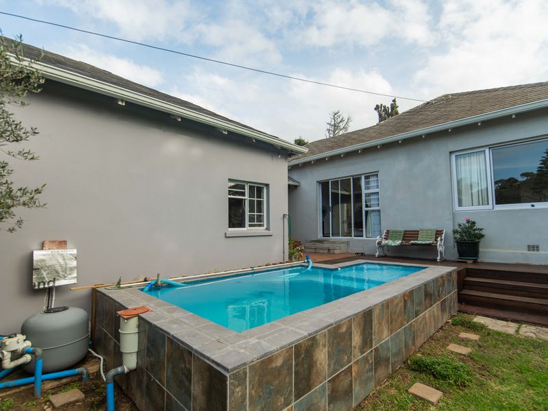 A raised swimming pool with tiled surround, adjacent to a timber deck and the rear exterior of the house.