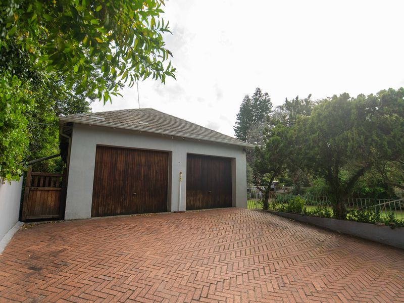 A detached double garage featuring timber doors and a brick-paved driveway, set within a landscaped garden area.