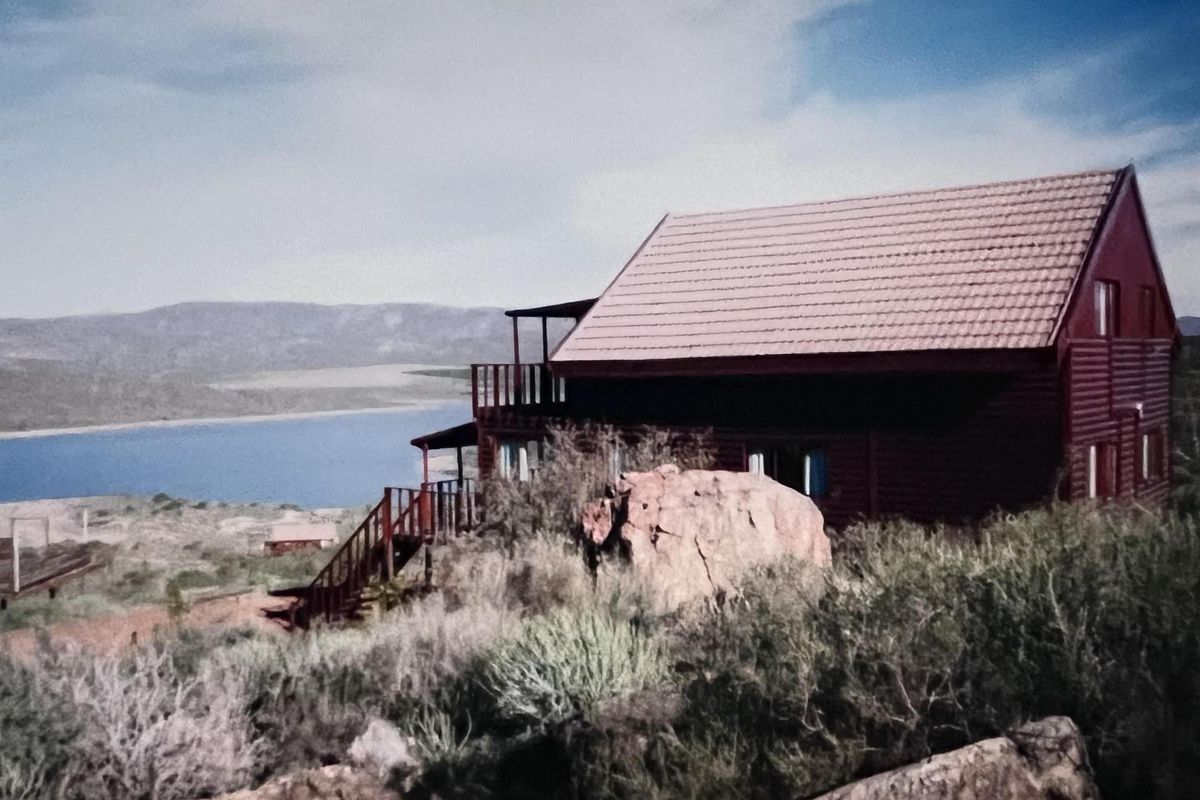 A rustic timber-clad house featuring a balcony and staircase, set in a natural landscape with scenic water views.