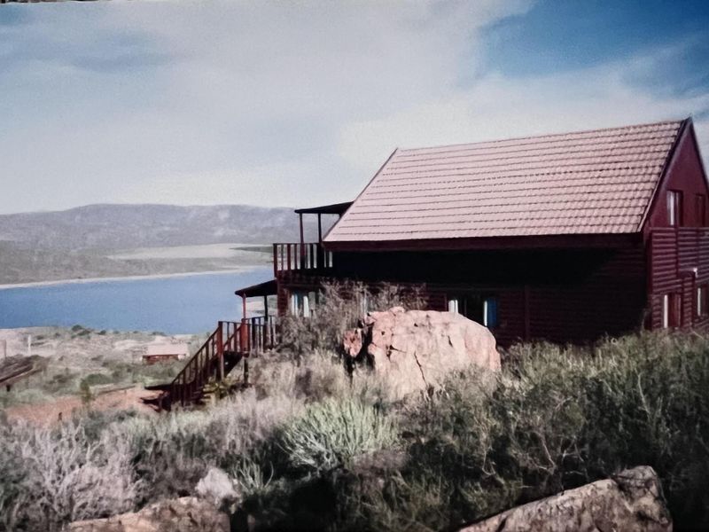 A rustic timber-clad house featuring a balcony and staircase, set in a natural landscape with scenic water views.