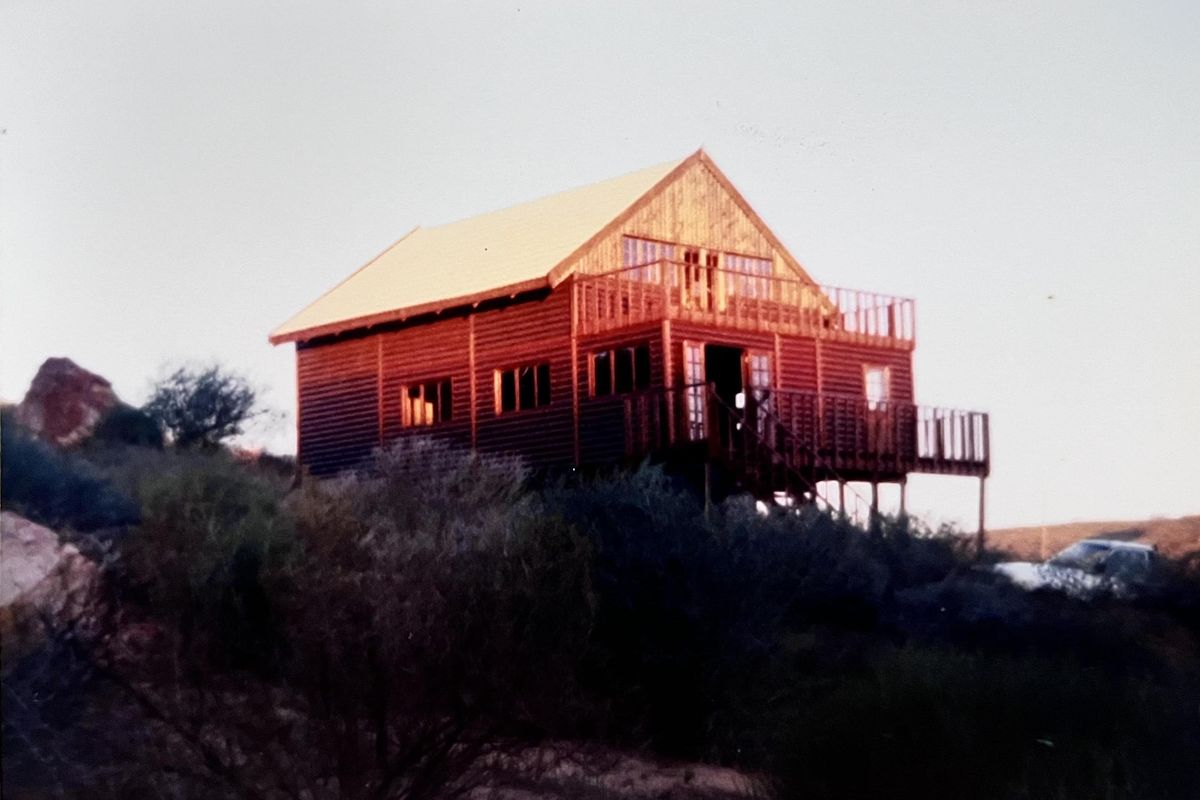 A rustic timber cabin featuring a raised deck and balcony, set in a natural landscape.