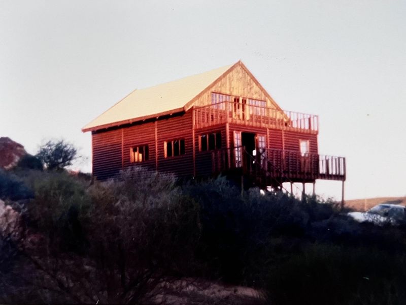 A rustic timber cabin featuring a raised deck and balcony, set in a natural landscape.