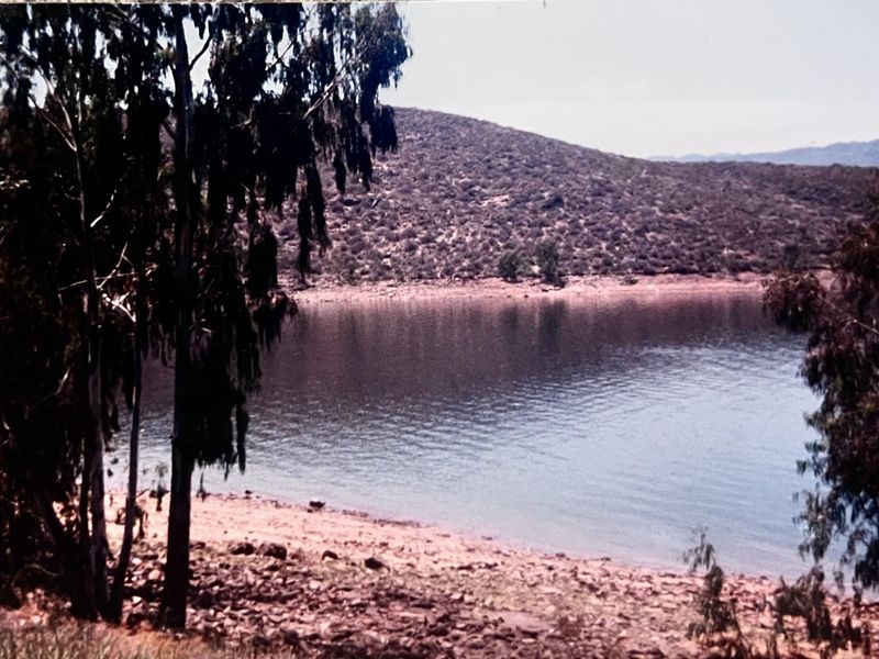 A scenic view of a natural lake or reservoir surrounded by hills and trees.