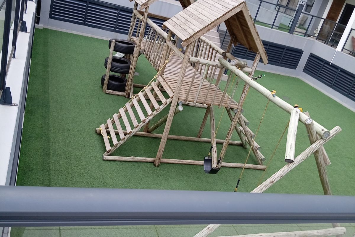 A well-maintained communal outdoor area featuring artificial turf, paved sections, and metal safety railings within an apartment complex.