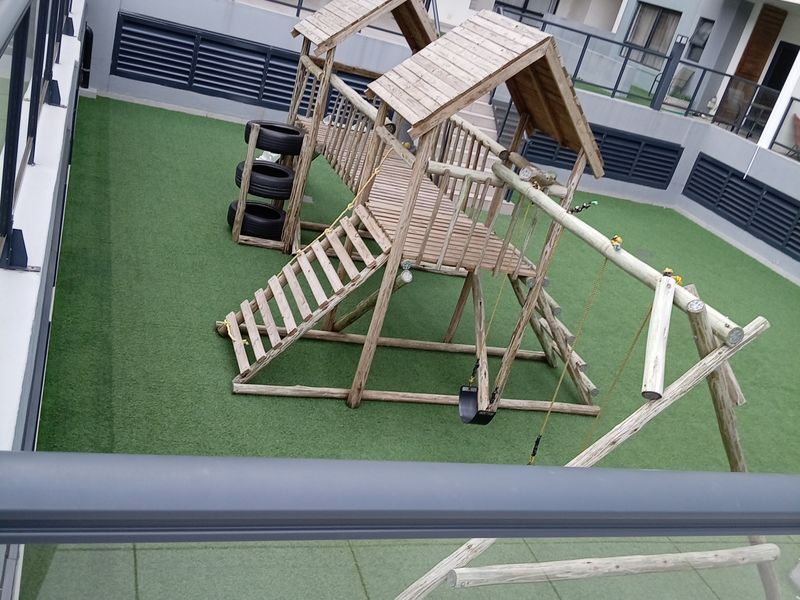 A well-maintained communal outdoor area featuring artificial turf, paved sections, and metal safety railings within an apartment complex.