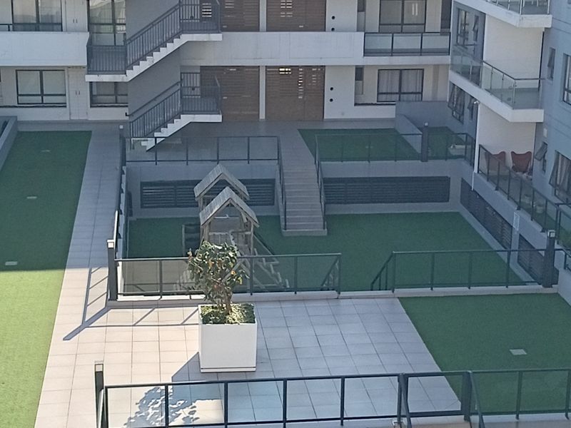 Elevated view of the apartment complex courtyard featuring a swimming pool, paved patio areas, artificial lawn, and communal staircases.
