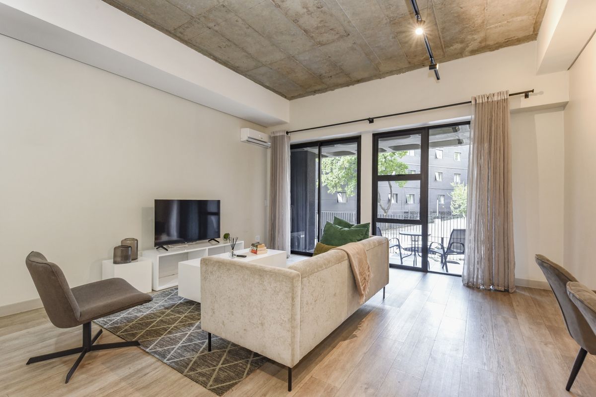 Modern living room featuring an exposed concrete ceiling, track lighting, and large sliding glass doors that provide access to an outdoor patio area.