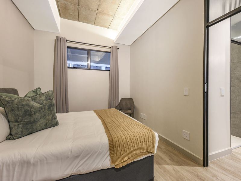 Modern bedroom featuring a unique exposed concrete ceiling detail, laminate flooring, and direct access to an en-suite bathroom.