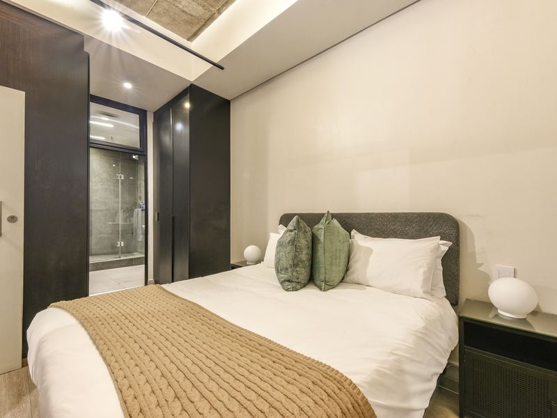 Modern bedroom featuring built-in cupboards, exposed concrete ceiling details, and direct access to an en-suite bathroom.