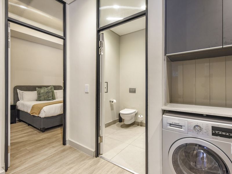Modern hallway featuring built-in cabinetry with integrated laundry appliance, stone countertop, and access to a bedroom and bathroom with stylish black-framed glass doors.