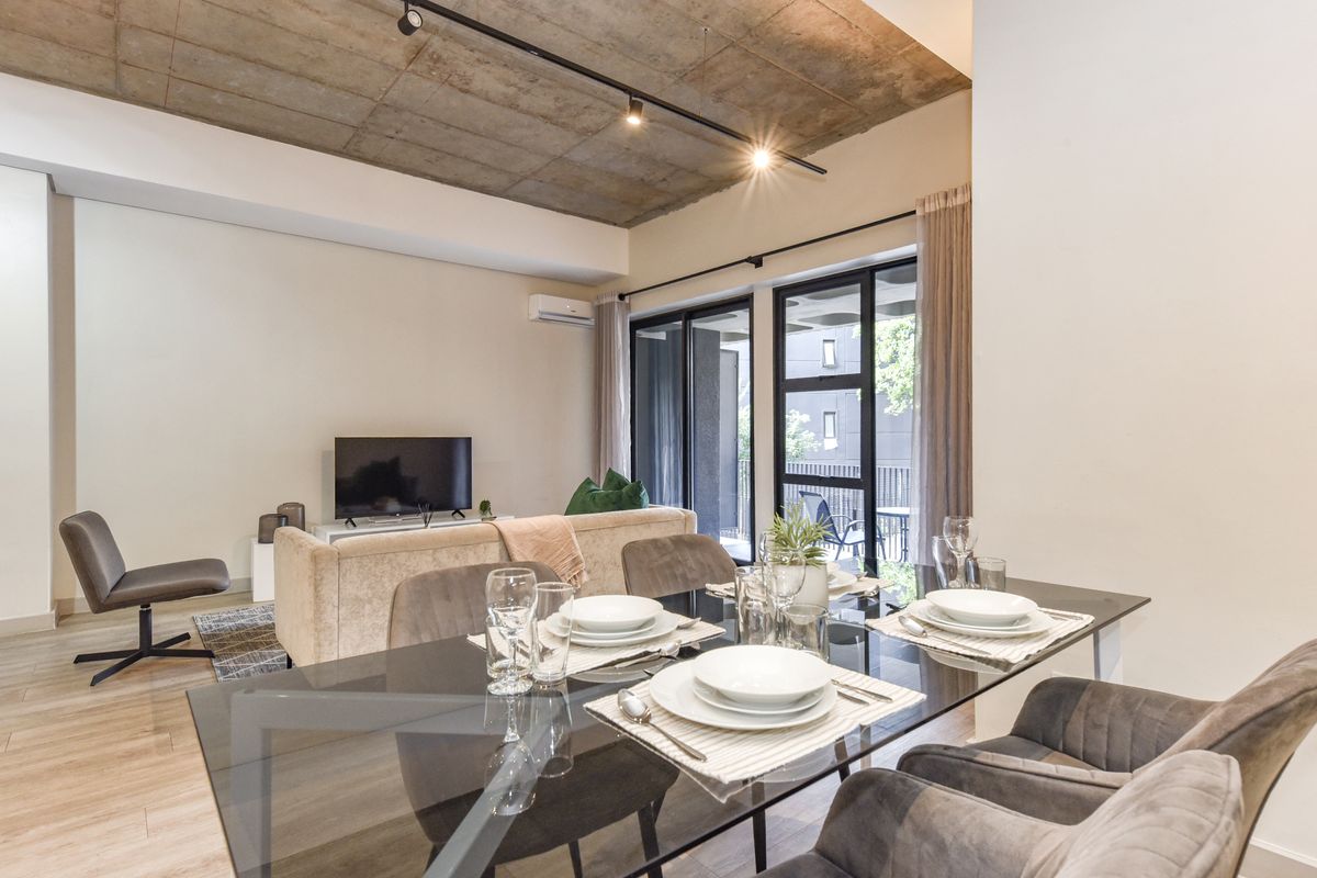 Modern open-plan living and dining area featuring an exposed concrete ceiling, track lighting, and large sliding glass doors leading to a balcony.