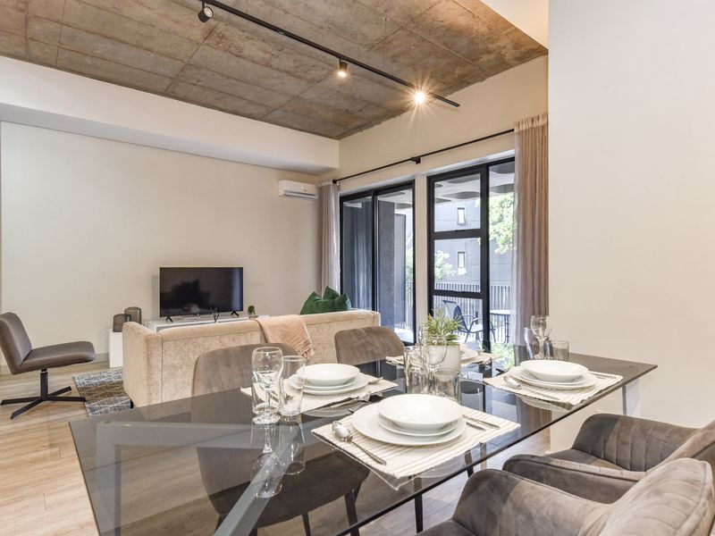Modern open-plan living and dining area featuring an exposed concrete ceiling, track lighting, and large sliding glass doors leading to a balcony.