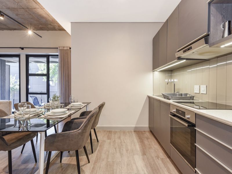 Modern open-plan kitchen and dining area featuring sleek cabinetry, integrated appliances, exposed concrete ceilings, and direct access to a balcony through sliding glass doors.