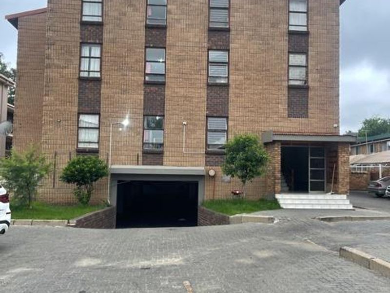 Front elevation of a multi-story brick apartment building featuring an underground parking entrance and a paved driveway area.