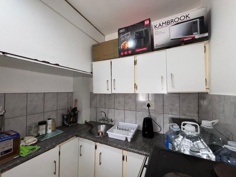 A compact kitchen featuring built-in cabinetry, a stainless steel sink, and tiled backsplash, currently showing signs of wear and requiring cosmetic updates.