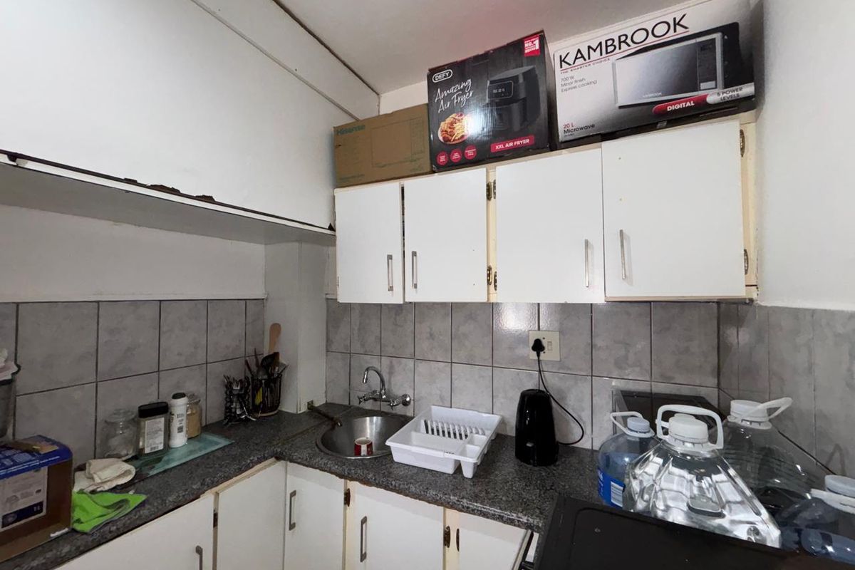 A compact kitchen featuring built-in cabinetry, a stainless steel sink, and tiled backsplash, currently showing signs of wear and requiring cosmetic updates.