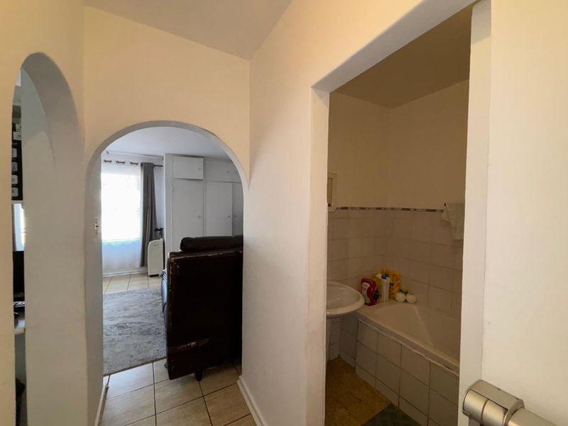 A hallway view showing an arched entryway leading to a living area and a bathroom featuring a pedestal basin and built-in bathtub.