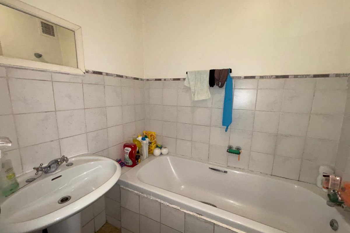 A functional bathroom featuring a pedestal washbasin, a built-in bathtub, and tiled walls. The space would benefit from cosmetic updates and modern finishes.