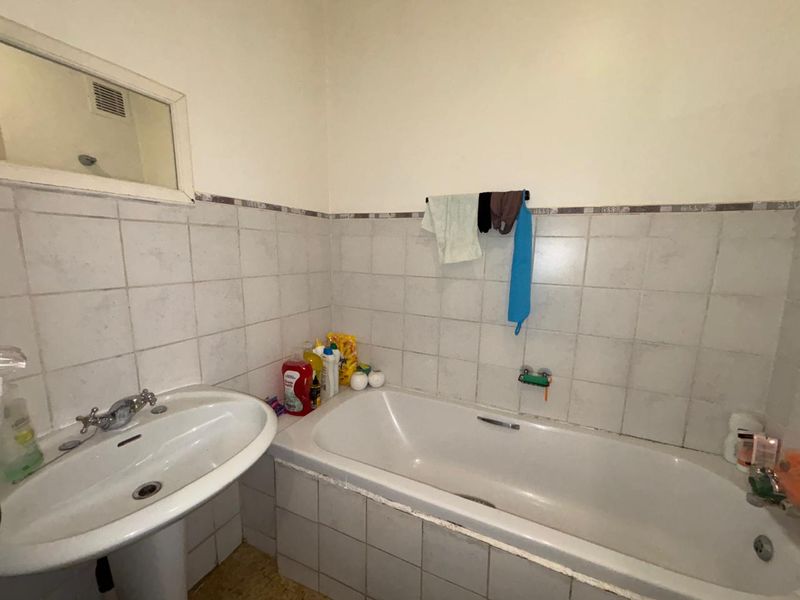 A functional bathroom featuring a pedestal washbasin, a built-in bathtub, and tiled walls. The space would benefit from cosmetic updates and modern finishes.