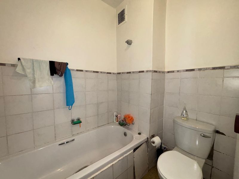 A functional bathroom featuring a standard bathtub, toilet, and tiled wall finishes, currently showing signs of wear and requiring cosmetic updates.
