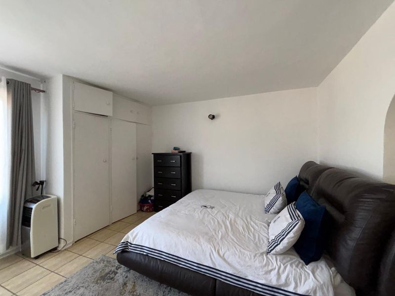 A bedroom featuring tiled flooring and built-in storage cupboards, providing a functional and neutral space.