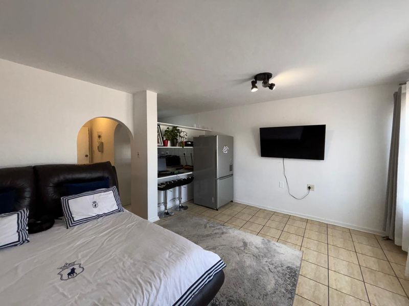 A bedroom featuring tiled flooring, an arched entryway, and a built-in breakfast bar area with overhead spotlighting.
