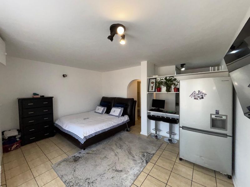 A bedroom featuring tiled flooring, a built-in shelving unit with a desk area, and an archway leading to an adjacent space.