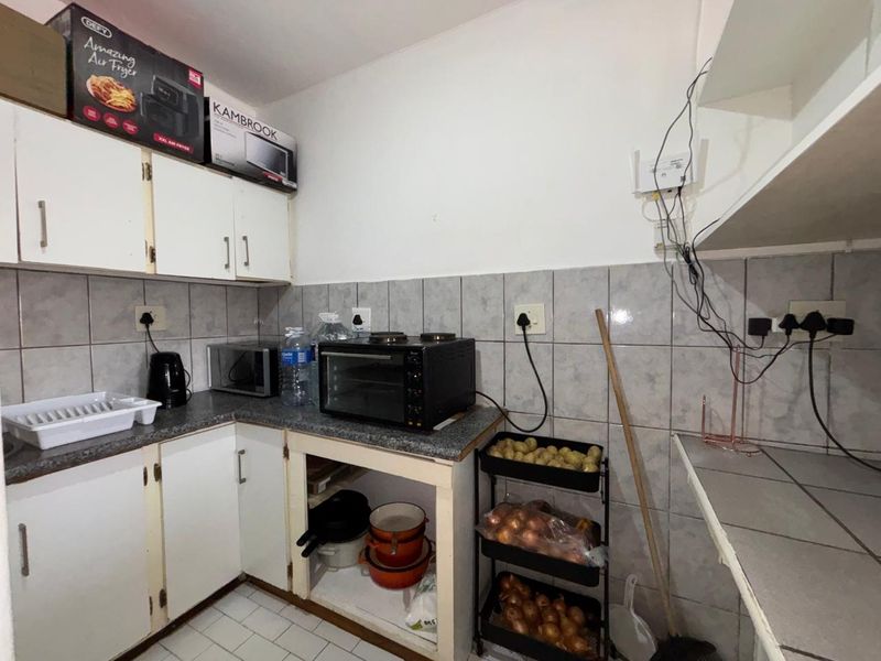 A functional scullery area featuring built-in cabinetry, tiled backsplash, and laminate countertops, requiring minor repairs and cable management.