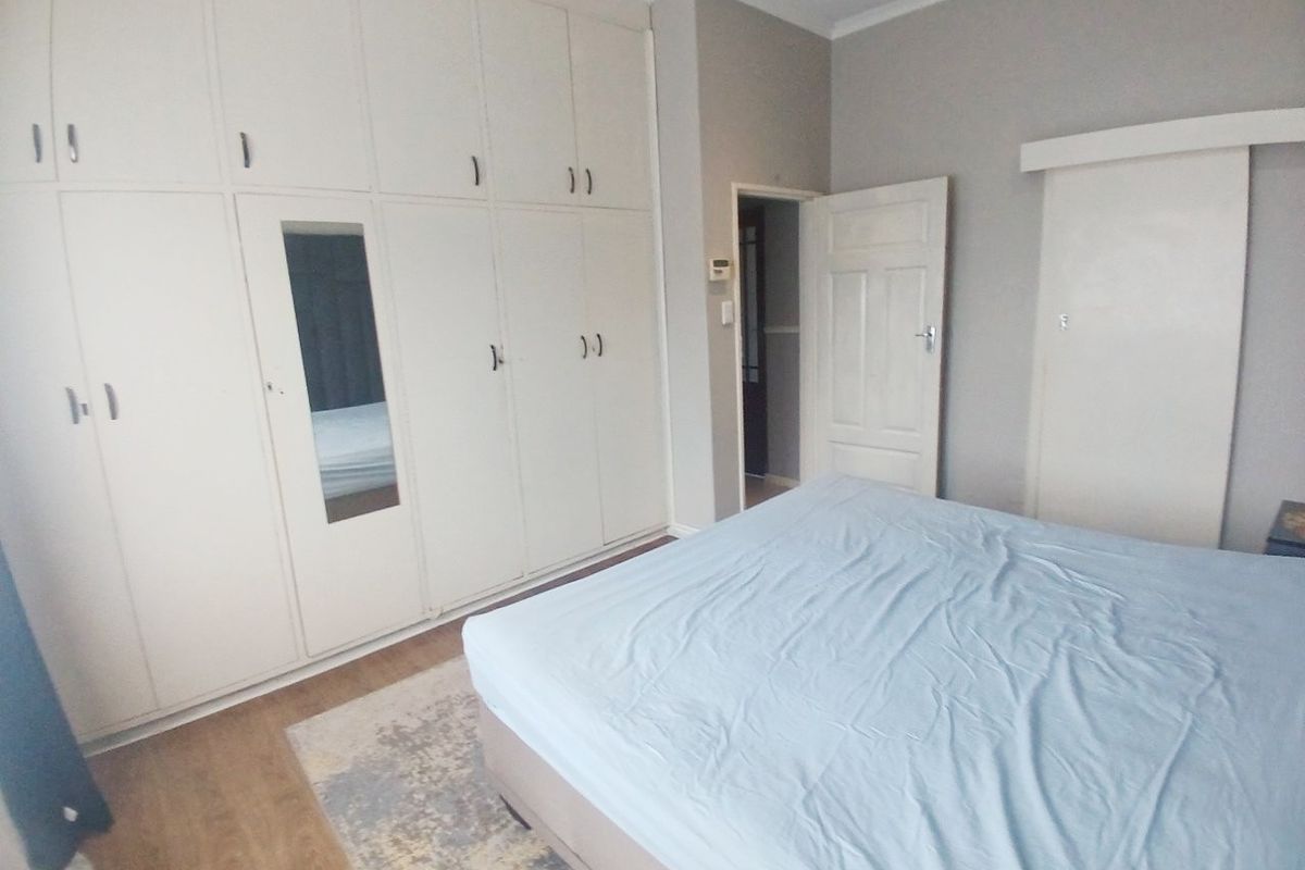 A well-lit bedroom featuring extensive built-in cupboard storage, laminate flooring, and neutral wall finishes.