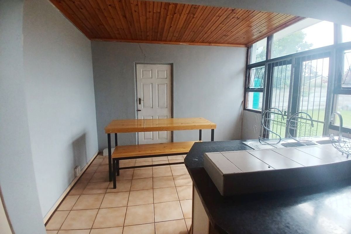 A functional kitchen area featuring tiled flooring, a timber ceiling, and a built-in counter with sink, requiring some cosmetic attention to the wall plaster.