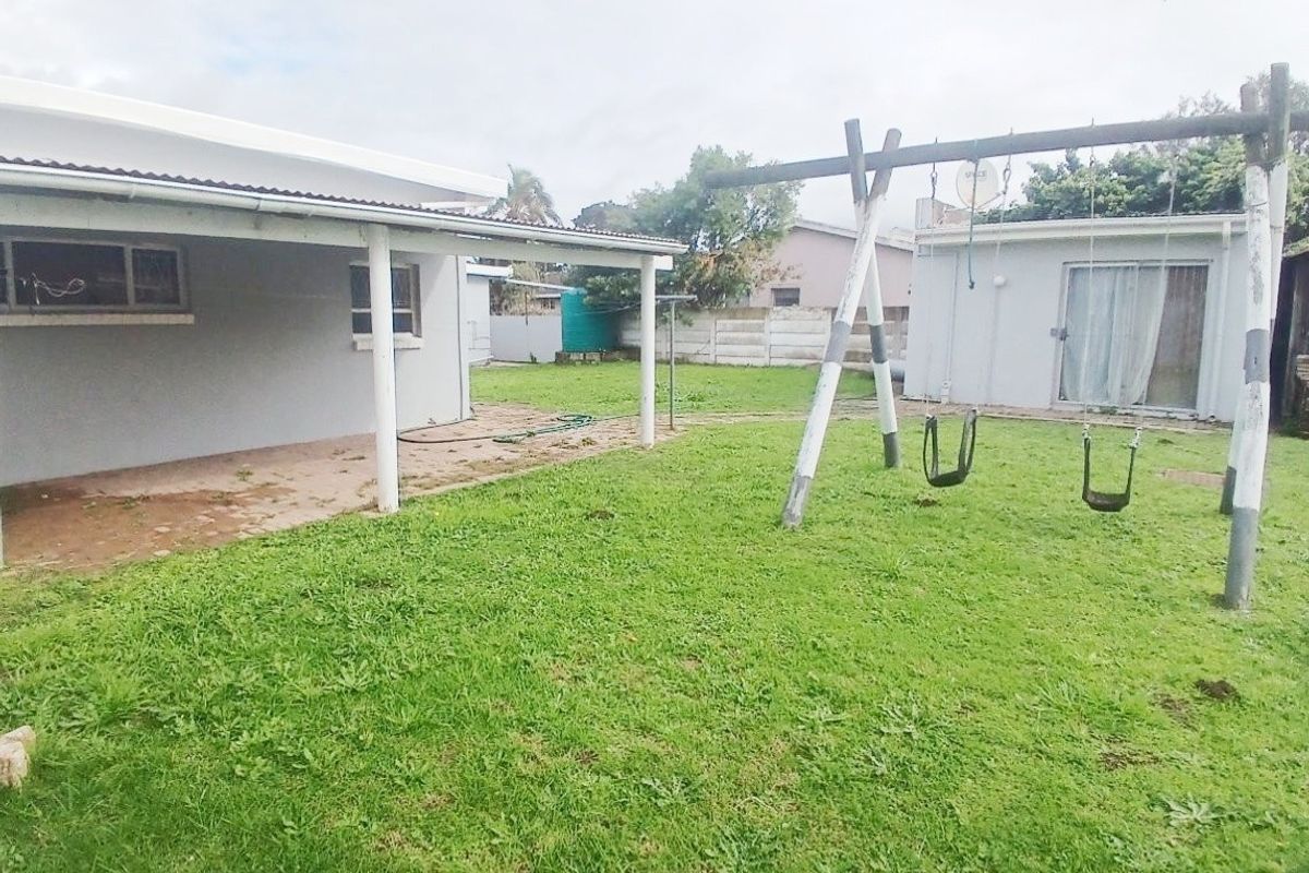 Rear garden view featuring a covered patio area, concrete slab flooring, and a surrounding precast concrete boundary wall.