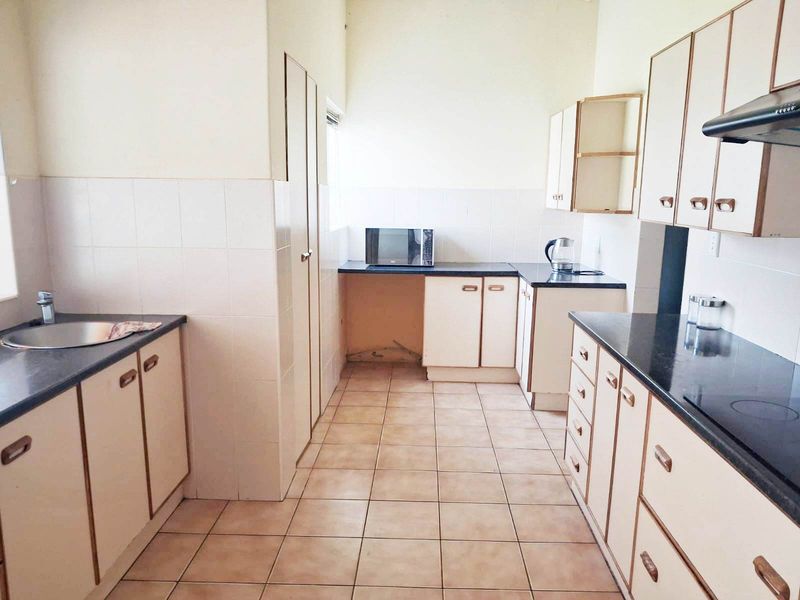 A functional kitchen featuring laminate cabinetry, dark countertops, ceramic tile flooring, and a built-in pantry, offering potential for modernization and cosmetic updates.