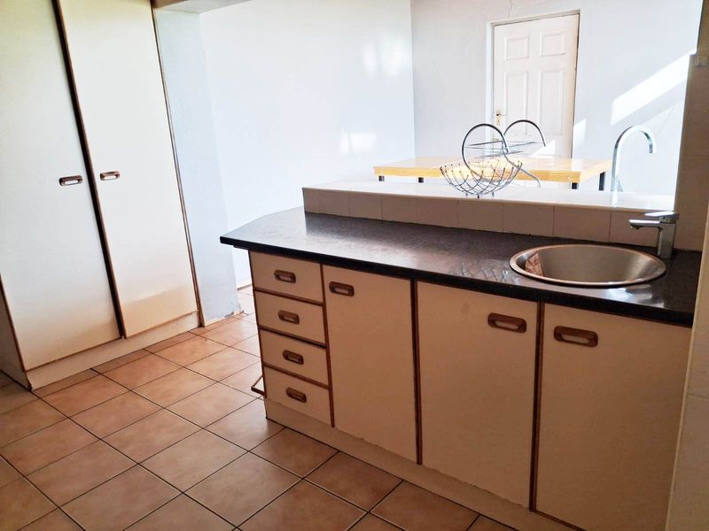 A functional kitchen area featuring built-in cabinetry, a laminate countertop with an integrated stainless steel sink, and tiled flooring.
