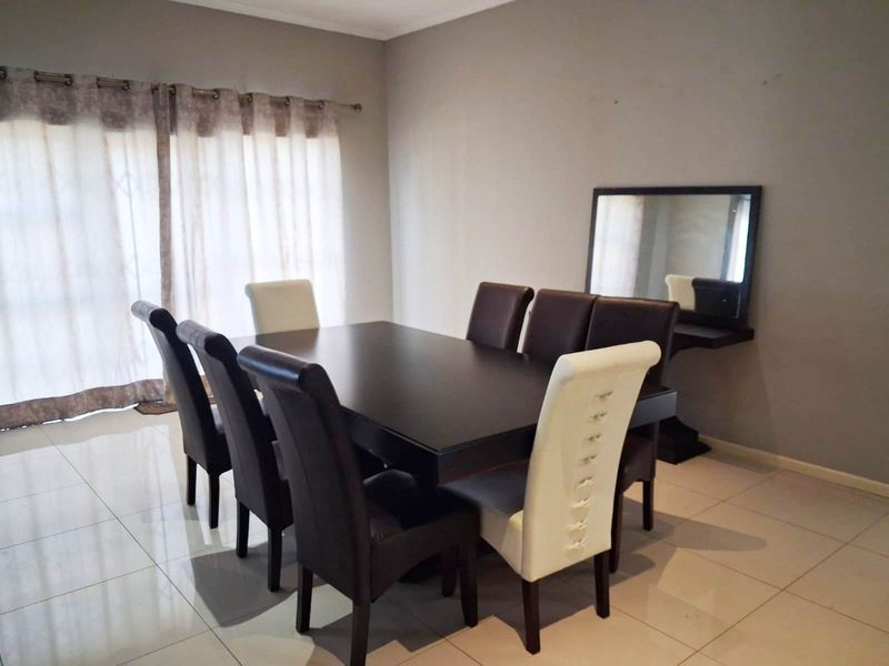 A dining room featuring neutral tiled flooring, a sliding glass door for natural light, and a wall-mounted mirror.