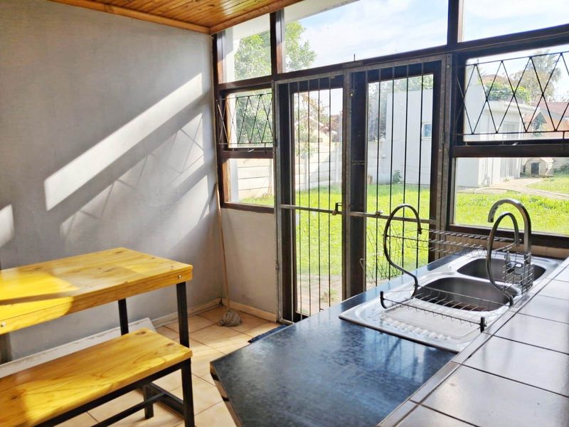 A functional scullery area featuring a double sink, tiled flooring, and a timber ceiling, with direct access to the rear garden through a security gate.