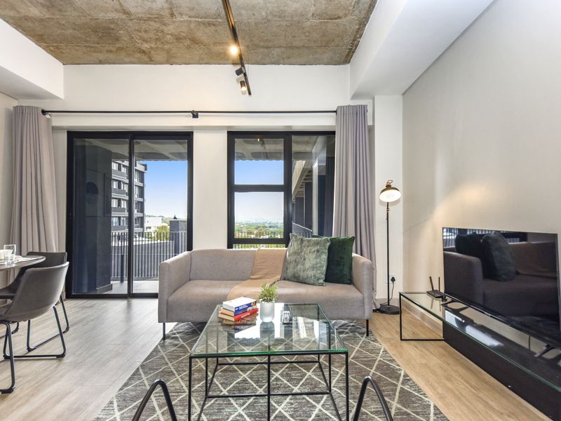 Modern open-plan living area featuring an exposed concrete ceiling, track lighting, and large sliding glass doors leading to a private balcony.
