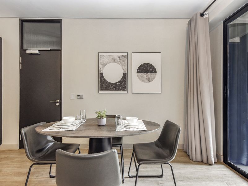 A modern dining area featuring laminate flooring, a sleek dark door with a transom window, and a large sliding glass door with floor-to-ceiling curtains.