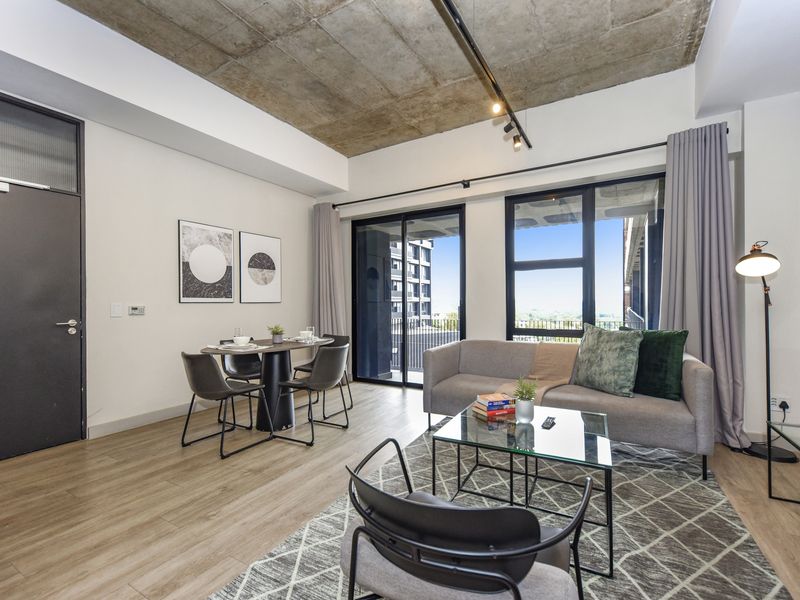 Modern open-plan living and dining area featuring an exposed concrete ceiling, track lighting, and large sliding doors leading to a balcony.