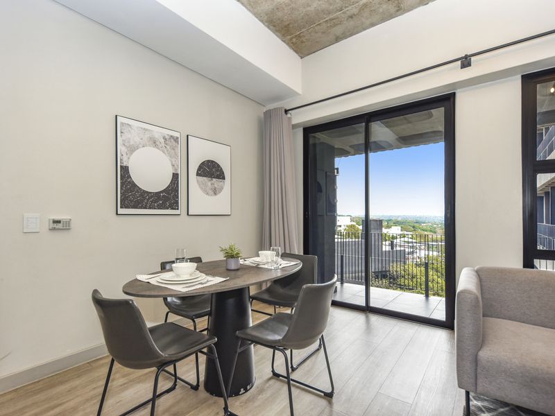 Modern open-plan living area featuring exposed concrete ceilings, laminate flooring, and large sliding glass doors opening onto a private balcony with scenic views.