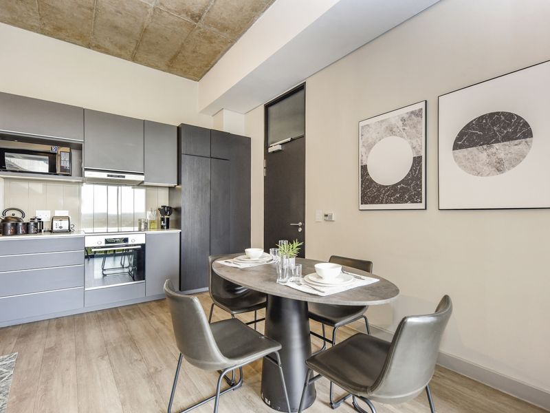 Modern open-plan kitchen and dining area featuring sleek grey cabinetry, integrated appliances, laminate flooring, and a striking exposed concrete ceiling.